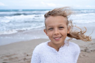 Child near water, wind, white sweater