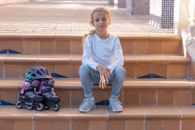 Kid sitting on the stairs, wearing rollers, Child helmet for rollers, pretty little girl learning to roller skate . High quality photo