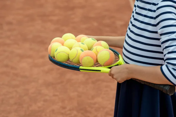 Çocuk tenisçi. Raket, bacak ve top. Tenis kulübündeki çocuklar için yaz etkinlikleri. Tenis kortunda küçük bir kızın kırpılmış görüntüsü. Atletik çocuk tenis topuna raketle vuruyor.