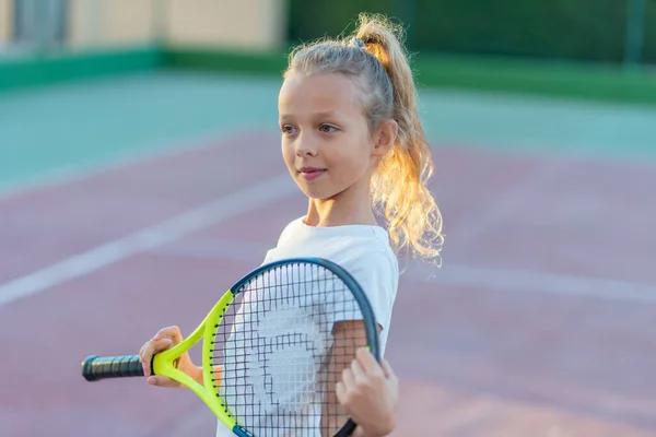 Çocuk tenisçi. Raket, bacak ve top. Tenis kulübündeki çocuklar için yaz etkinlikleri. Tenis kortunda küçük bir kızın kırpılmış görüntüsü. Atletik çocuk tenis topuna raketle vuruyor.