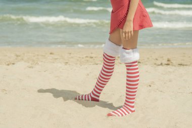 Legs child girl wearing Santa Claus socks on beach near sea, legs and skirt. Xmas vacation High quality photo clipart