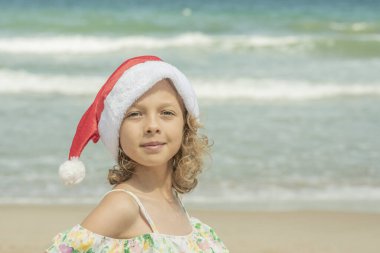Plajda deniz kenarında Noel Baba şapkası takan çocuk, yüzü büyük. Xmas tatili Yüksek kaliteli fotoğraf