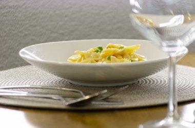 Bezelyeli bir kase kremalı makarna, arka planda şarap kadehiyle servis edilen bir servis altlığı. Makarnanın görüntüsü, dokusunu ve rengini vurguluyor..