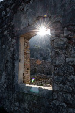 Güneş ışığı, arka planda manzaralı dağların olduğu antik bir harabenin taş penceresinden akıyor. Tarihle doğanın çarpıcı bir karışımı..