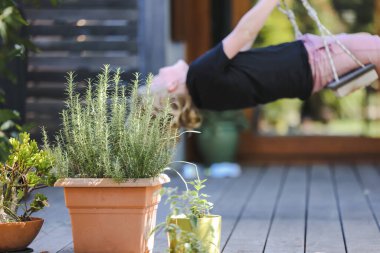 Arka güvertede yetişen biberiye bitkisi ve arka planda salıncakta sallanan çocuk.