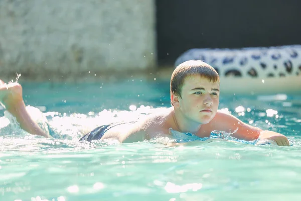 Adolescent boy swimming on boogie board in backyard pool