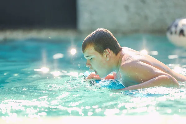 Adolescent boy swimming on boogie board in backyard pool