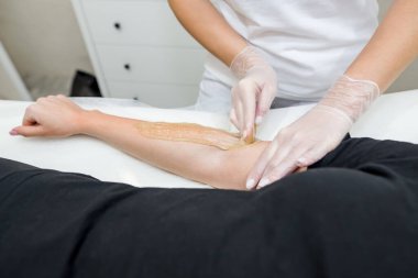 Şeker macunu tüy yolma prosedürü - karıştırma. Kozmetik uzmanı genç bir kadının eline şeker yapıştırıcısı sürüyor..