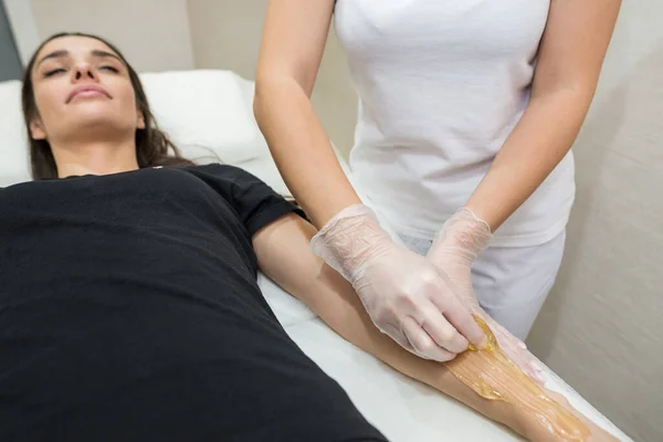 Sugar paste hair removal procedure - shugaring. Cosmetologist applies sugar paste to the hand of a young woman.Depilation of female hands in a beauty parlor.