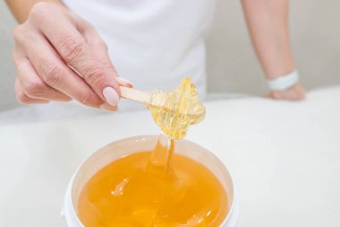 Saç çıkarma prosedürü için elinde bir kova şekerle bir kadın güzellik uzmanının yakın plan fotoğrafı. Tüy dökme, epilasyon, ağda, karıştırma kavramı..