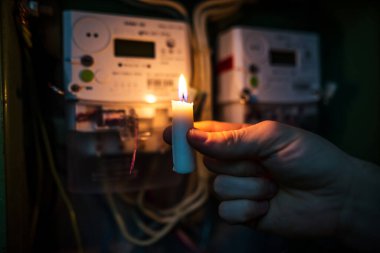 Evdeki elektrik kesintisi sırasında elektrik sayacının yanında mum ışığı parlıyor. Elektrik yok. El yanan bir mum tutuyor..