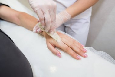 Şeker macunu tüy yolma prosedürü - karıştırma. Kozmetik uzmanı genç bir kadının eline şeker yapıştırıcısı sürüyor. Kadın elinin güzellik salonunda dezenfekte edilmesi..