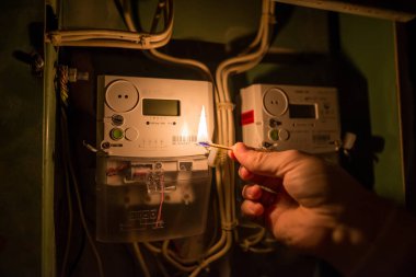 Karanlıkta bir adamın eli ev elektrik sayacını okumak için yanan bir kibrit tutuyor. Elektrik kesintisi, enerji krizi veya karartma, kavramsal görüntü.