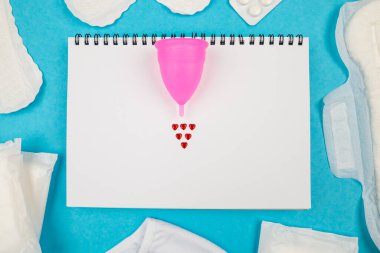 Not defterinde fotoğraf bardağı, mavi arka planda kadın pedleri. Kadın adet dönemi kavramı..