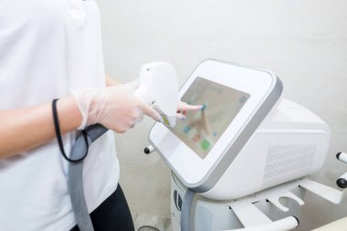 Güzellik salonunda kozmetik uzmanının eli modern bir lazer cihazını ayarlıyor. Lazer darbeleriyle deri temizleme prosedürü. Fototermoliz süreci, deriyi ısıtır. Donanım