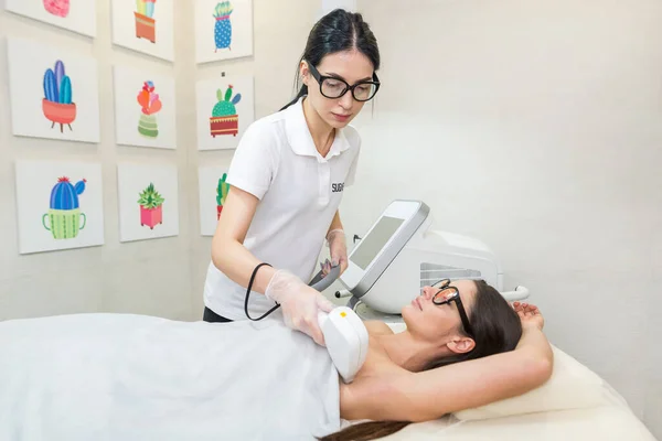 Laser hair removal and cosmetology in a beauty salon. Hair removal procedure. The concept of laser hair removal, cosmetology, spa and hair removal. Beautiful brunette woman getting armpit hair removal