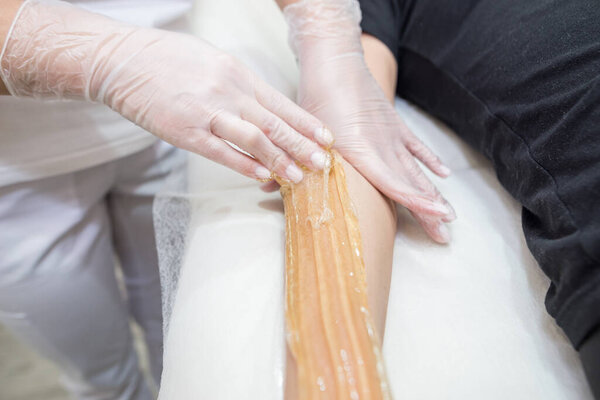 Sugar paste hair removal procedure - shugaring. Cosmetologist applies sugar paste to the hand of a young woman.