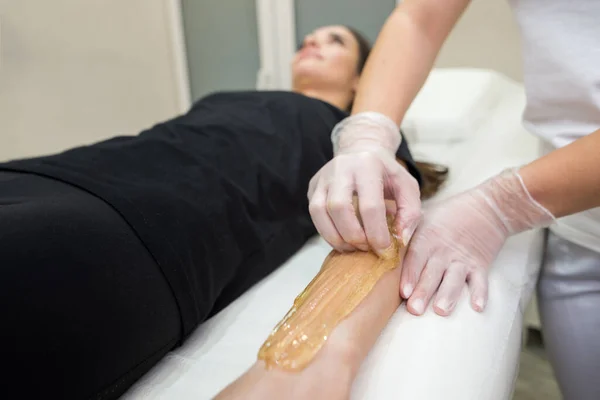 Sugar paste hair removal procedure - shugaring. Cosmetologist applies sugar paste to the hand of a young woman.Depilation of female hands in a beauty parlor.