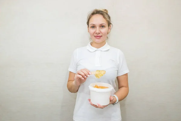 portrait of a woman with a jar of sugar paste for sugaring.Beautician holding a jar of sugar paste for shugaring on a white background