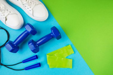 Spor aksesuarları konsepti. Lastik bandın, halat atlama halatlarının ve beyaz spor ayakkabıların iki ton yeşil ve mavi arka planda, boş arkaplan, üst görünüm