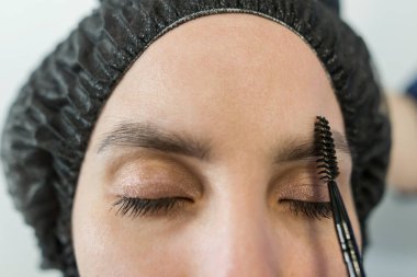 Makyaj yapmadan önce genç ve güzel bir kadının kaşlarını tarıyor. Makyaj konsepti, kaş şekli modelleme.