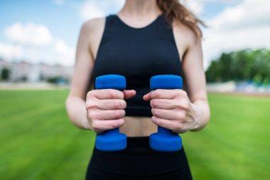 Stadyuma dambıllarla spor yapmaya giden ince, atletik bir genç kızın kesilmiş fotoğrafı. Dambılı atletik kadın dışarıda..