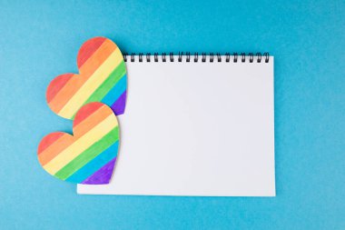 LGBT sembolü, mavi arkaplan, haklar ve cinsiyet eşitliği üzerinde boş bir not defteri olan gökkuşağı kalpleri. kopyalama alanı. Metin için yer.