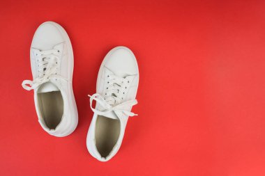 Kırmızı arkaplanda beyaz spor ayakkabılarının üst görünümü