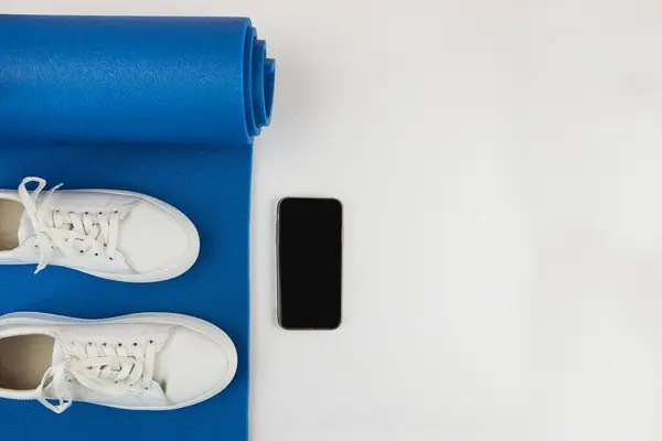 健康的生活方式的概念 白色运动鞋 智能手机 蓝色运动垫及其他运动配件的全景照片 — 图库照片