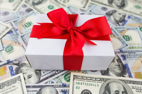 stock image White gift box with a red bow on a money background.