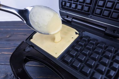 Ev yapımı Belçika Waffle 'ı yapma süreci. Bir kadının eli Belçika Waffle 'ının hamurunu elektrikli waffle ızgarasının ısıtılmış panellerine kaşıklıyor..
