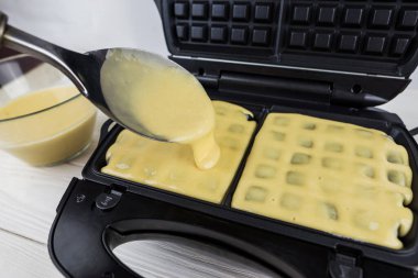Malzemeli modern waffle makinesi, ev yapımı Belçika waffle 'ı. Kadın Belçikalı waffle makinesinin üzerine hamur döküyor.