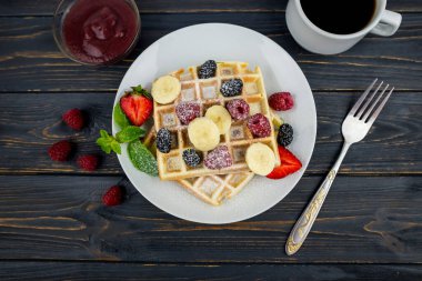 Koyu ahşap arka planda beyaz tabakta yaz meyveleri ve pudra şekerli Belçika waffleları. Kahvaltıda ya da öğle yemeğinde Belçika waffle 'ı