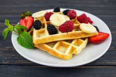 Koyu ahşap arka planda beyaz tabakta yaz meyveleri ve pudra şekerli Belçika waffleları. Kahvaltıda ya da öğle yemeğinde Belçika waffle 'ı