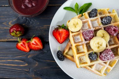 Koyu ahşap arka planda beyaz tabakta yaz meyveleri ve pudra şekerli Belçika waffleları. Kahvaltıda ya da öğle yemeğinde Belçika waffle 'ı