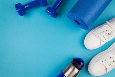 Spor aksesuarları konsepti. Mavi halterlerin, mavi spor paspasın, beyaz spor ayakkabıların ve diğer spor malzemelerinin fotoğrafı. Spor, spor, yoga, kilo kaybı, sağlıklı yaşam tarzı.