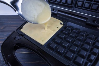 Malzemeli modern waffle makinesi, ev yapımı Belçika waffle 'ı. Kadın Belçikalı waffle makinesinin üzerine hamur döküyor.
