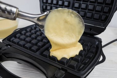 Malzemeli modern waffle makinesi, ev yapımı Belçika waffle 'ı. Kadın Belçikalı waffle makinesinin üzerine hamur döküyor.