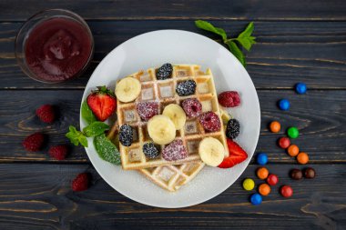 Koyu ahşap arka planda beyaz tabakta yaz meyveleri ve pudra şekerli Belçika waffleları. Kahvaltıda ya da öğle yemeğinde Belçika waffle 'ı