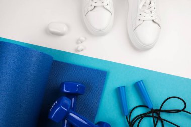 Spor aksesuarları konsepti. Mavi halterlerin, mavi spor minderlerinin ve mavi ve beyaz arka plandaki diğer spor ekipmanlarının en üstteki görüntüsü.