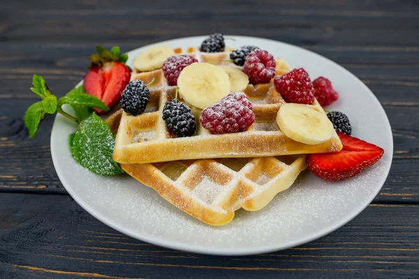 stock image Belgian waffles with summer berries and powdered sugar in a white plate on a dark wooden background. Sweet Belgian waffles for breakfast or lunch