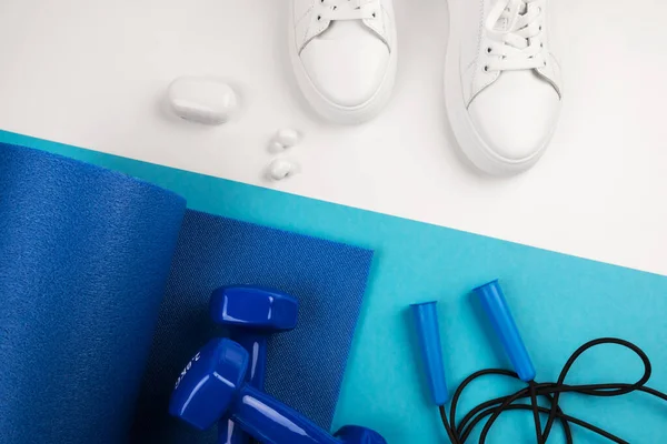 Spor aksesuarları konsepti. Mavi halterlerin, mavi spor minderlerinin ve mavi ve beyaz arka plandaki diğer spor ekipmanlarının en üstteki görüntüsü.