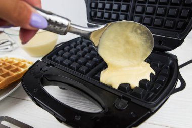 Malzemeli modern waffle makinesi, ev yapımı Belçika waffle 'ı. Kadın Belçikalı waffle makinesinin üzerine hamur döküyor.