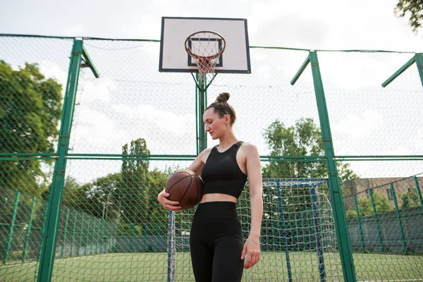 Young sports girl with a basketball on the basketball court outdoors, active weekend.