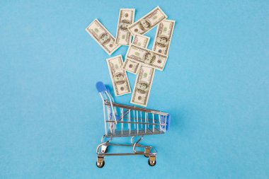 Dolarlar mavi arka planda el arabasında. Alışveriş, promosyon, indirim kavramı..