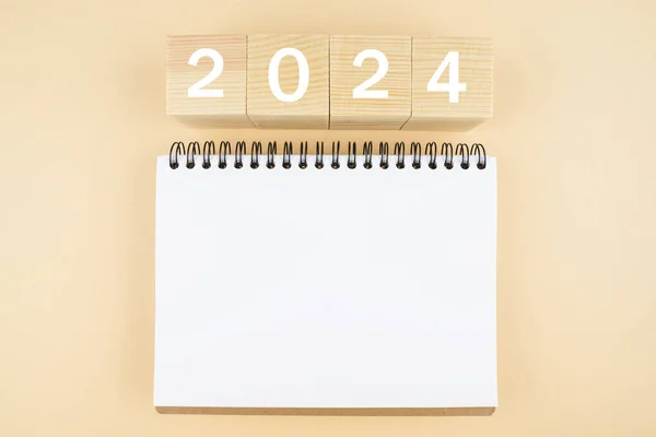 2024 time for new start. white paper and 2024 cubes. wooden table background. New Year plans for 2024, blank space on notepad, mockup calendar. Start new year 2024 with goal plan