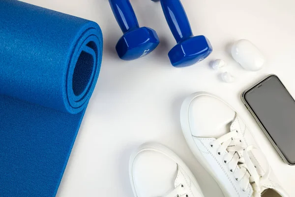 The concept of sports accessories. Photo of white sneakers, blue dumbbells and a blue exercise mat and other sports equipment.