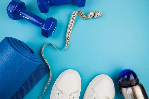 The concept of sports accessories. Photo of white sneakers, blue dumbbells and a blue exercise mat and other sports equipment.