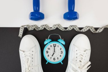Beyaz saatli dambıl spor ayakkabıları ve diğer spor aletlerinin en üstteki fotoğrafı. Yoga fitness spor zayıflama konsepti