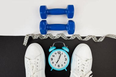 Beyaz saatli dambıl spor ayakkabıları ve diğer spor aletlerinin en üstteki fotoğrafı. Yoga fitness spor zayıflama konsepti